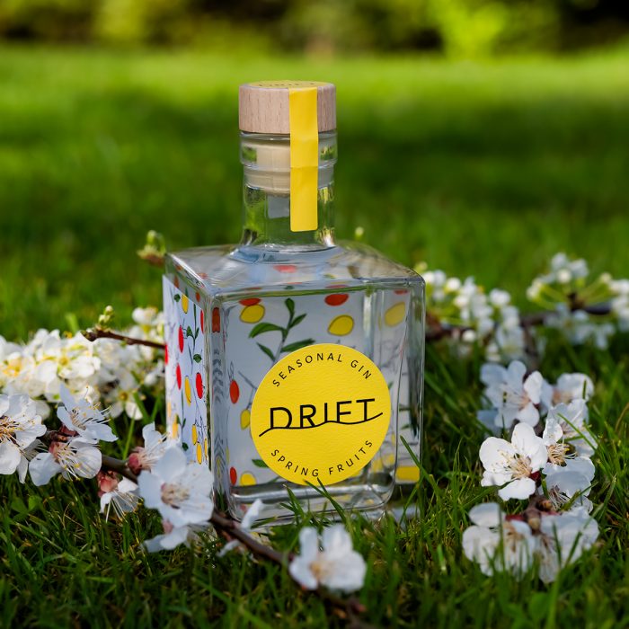350ml Drift Spring Fruits gin on green grass surrounded by apricot blossoms.