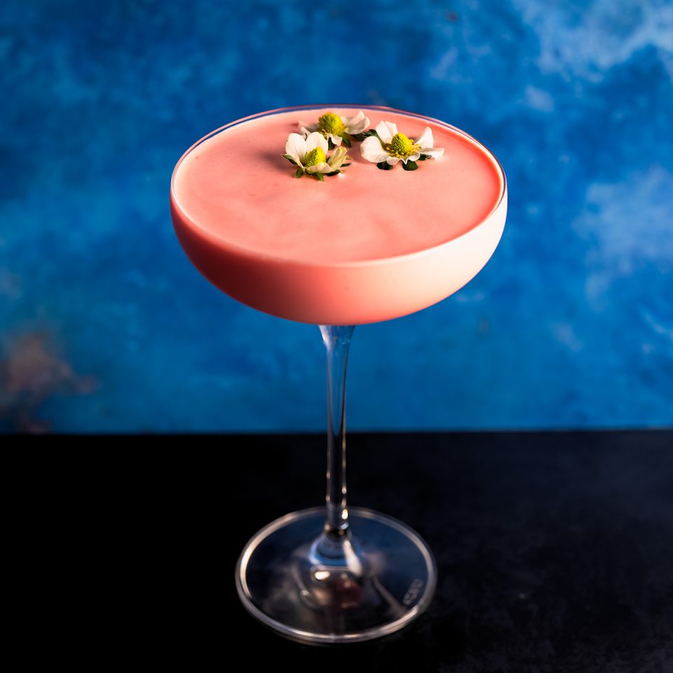 Drift Summer Dream is a pink creamy strawberry gin cocktail in a coupe glass, garnished with 3 strawberry flowers
